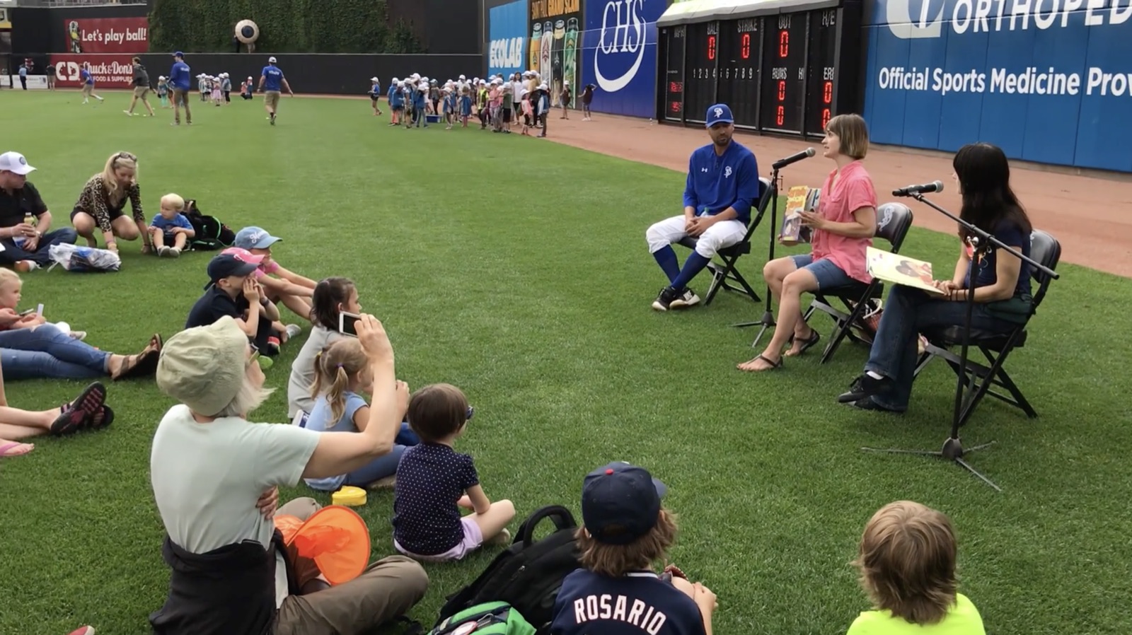 Stephanie Watson reading her book Best Friends in the Universe on the baseball field.